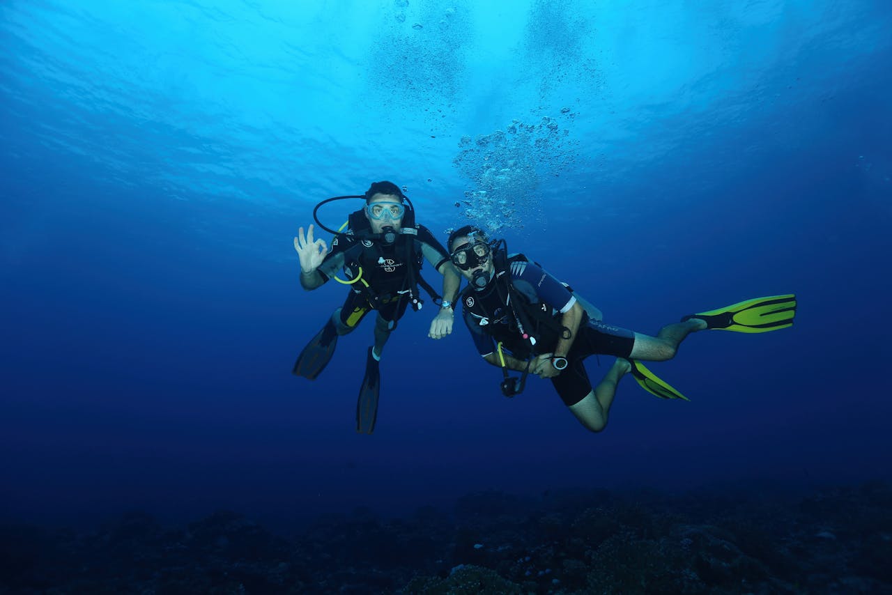 Two scuba divers with gear exploring the deep blue ocean, captured under natural light.