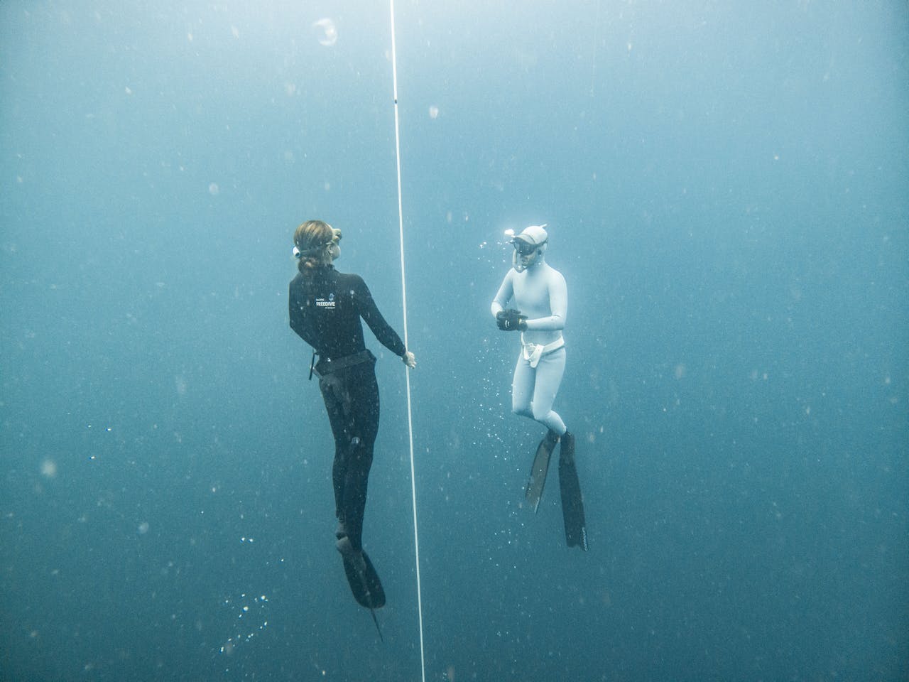 Two freedivers explore deep blue waters in Lombok, Indonesia, using guide rope for orientation.